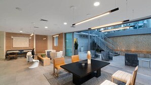 A modern indoor space with a black table, white and wooden chairs, a staircase, and a view of the outside.