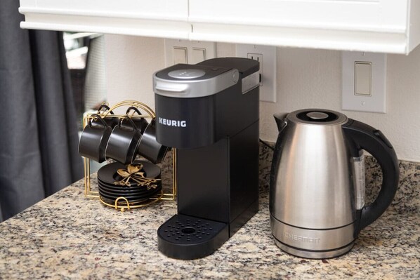 A coffee maker, a kettle, and a stack of black cups on a kitchen counter.