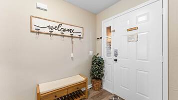 A hallway with a wooden bench, a welcome sign, a potted plant, and a white door.