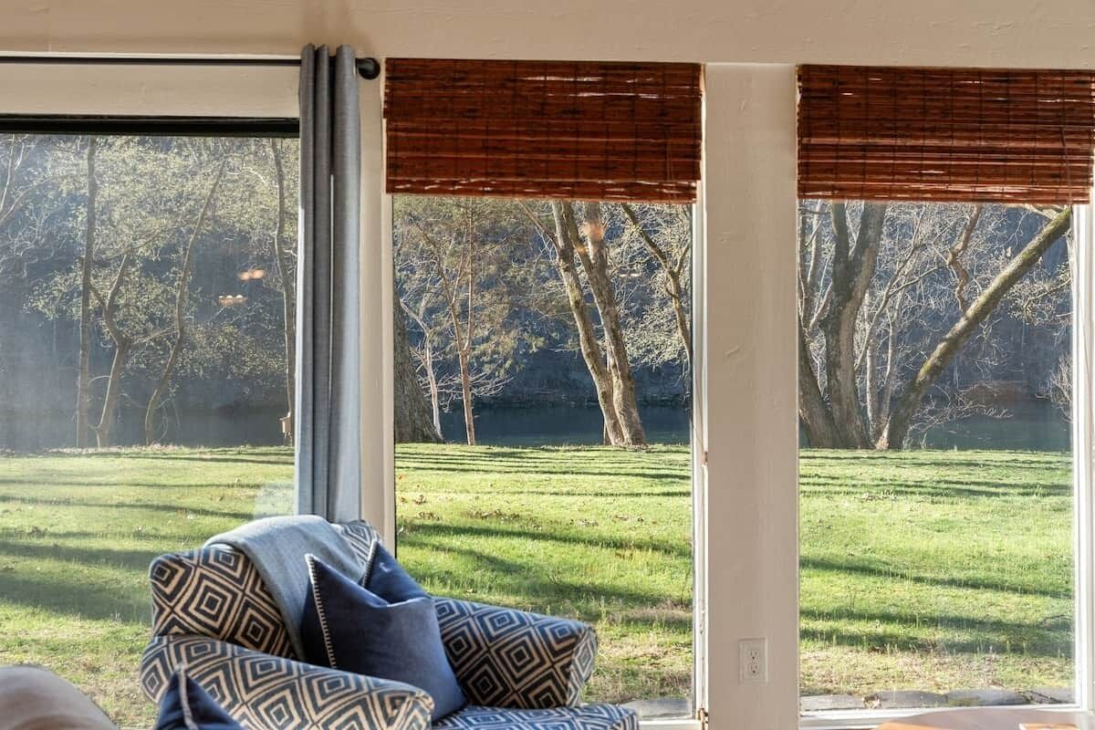 A room with a large window, a patterned sofa, and a view of a grassy area with trees.