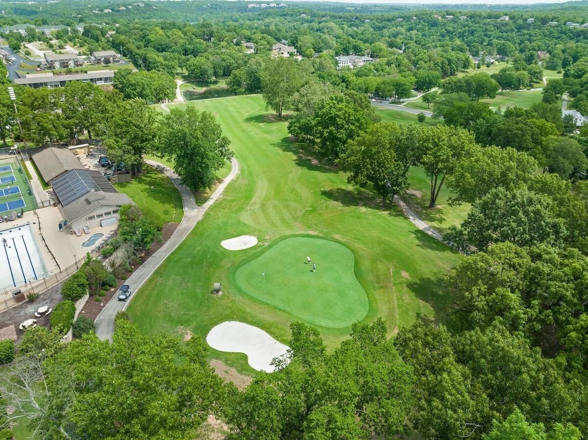 Vista aérea de un campo de golf con un putting green, búnkeres de arena y un club de campo con piscina.