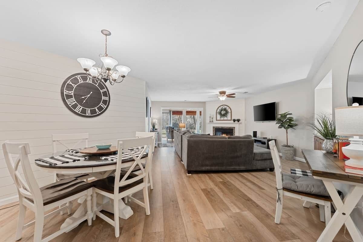 A modern living room with a fireplace, a dining area with a clock, and a television mounted on the wall.