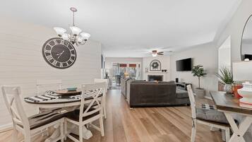 A modern living room with a fireplace, a dining area with a clock, and a television mounted on the wall.