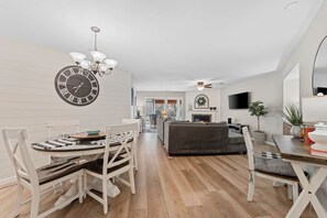 Un salon moderne avec une cheminée, un coin repas agrémenté d’une horloge et un téléviseur fixé au mur.