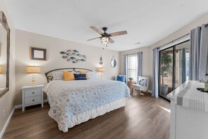 A bedroom with a bed, bedside tables, a ceiling fan, and a large window with curtains.