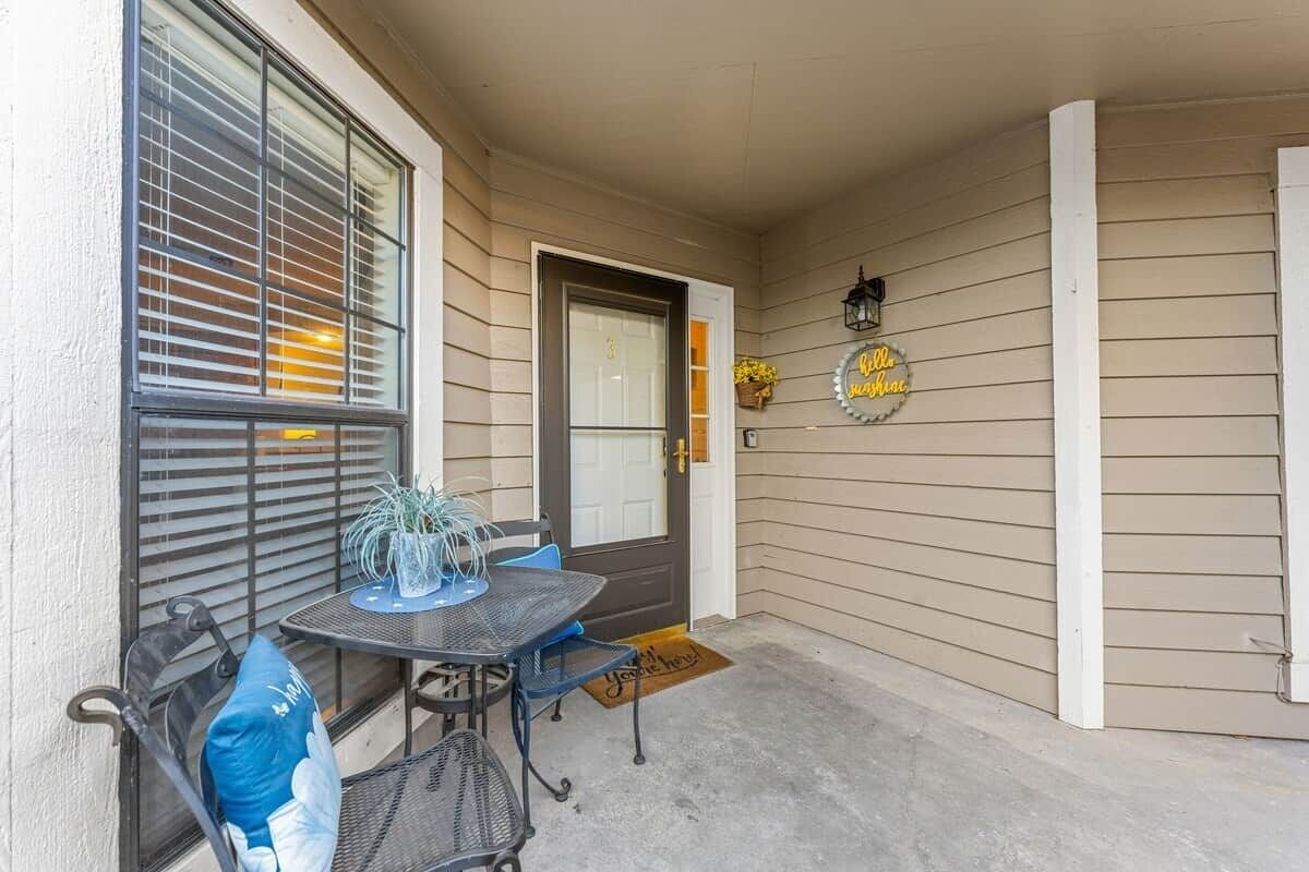 A covered porch with a table and chairs, a door, and a welcome mat.