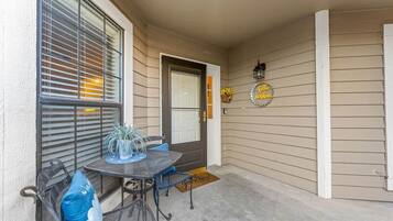 A covered porch with a table and chairs, a door, and a welcome mat.