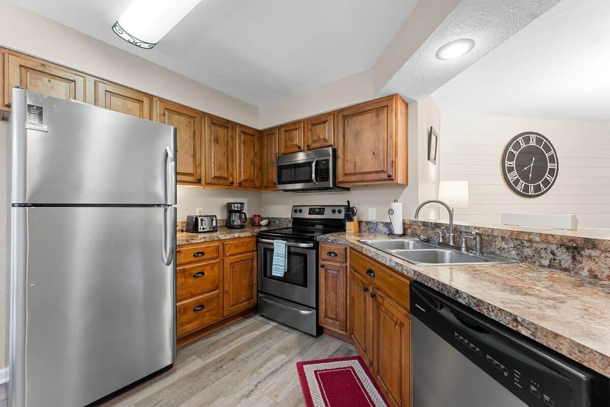 A kitchen with wooden cabinets, stainless steel appliances, granite countertops, and a clock on the wall.