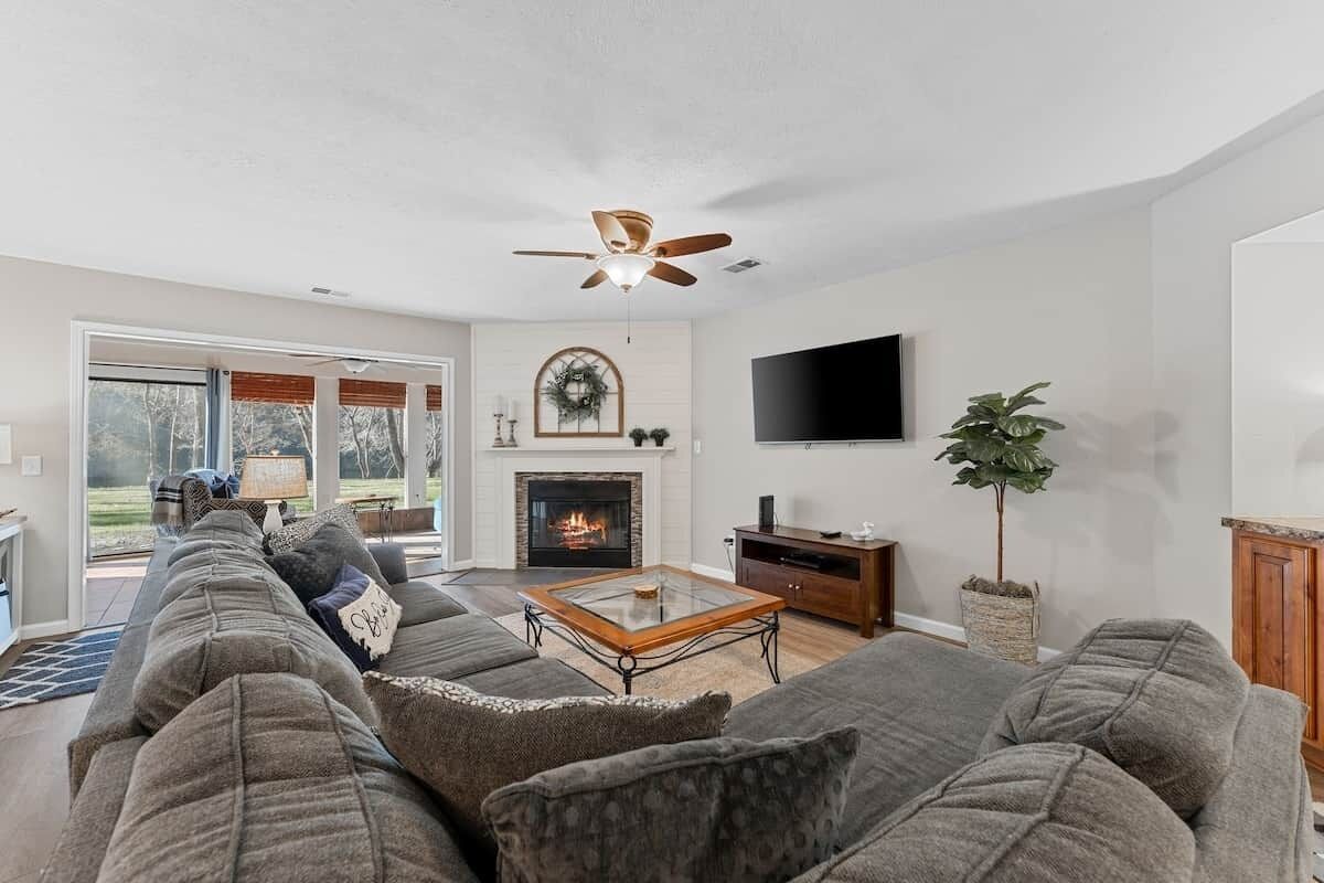 A living room with a fireplace, a ceiling fan, and a television mounted on the wall.