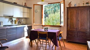 Eine Küche mit Esstisch, Stühlen, Schränken, einem Heizkörper und einem Fenster mit Blick auf Grünfläche.