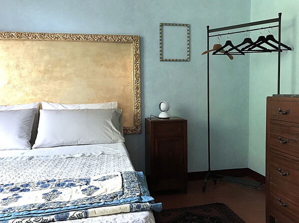 A bedroom with a bed, a dresser, a coat rack, and a wall-mounted mirror.