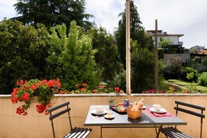An outdoor dining area with a table set for two, surrounded by greenery and flowers.