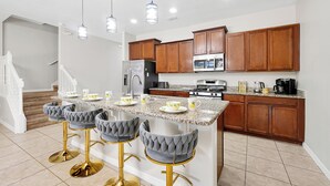 Una cocina moderna con una isla central, taburetes de bar, armarios de madera y electrodomésticos de acero inoxidable.
