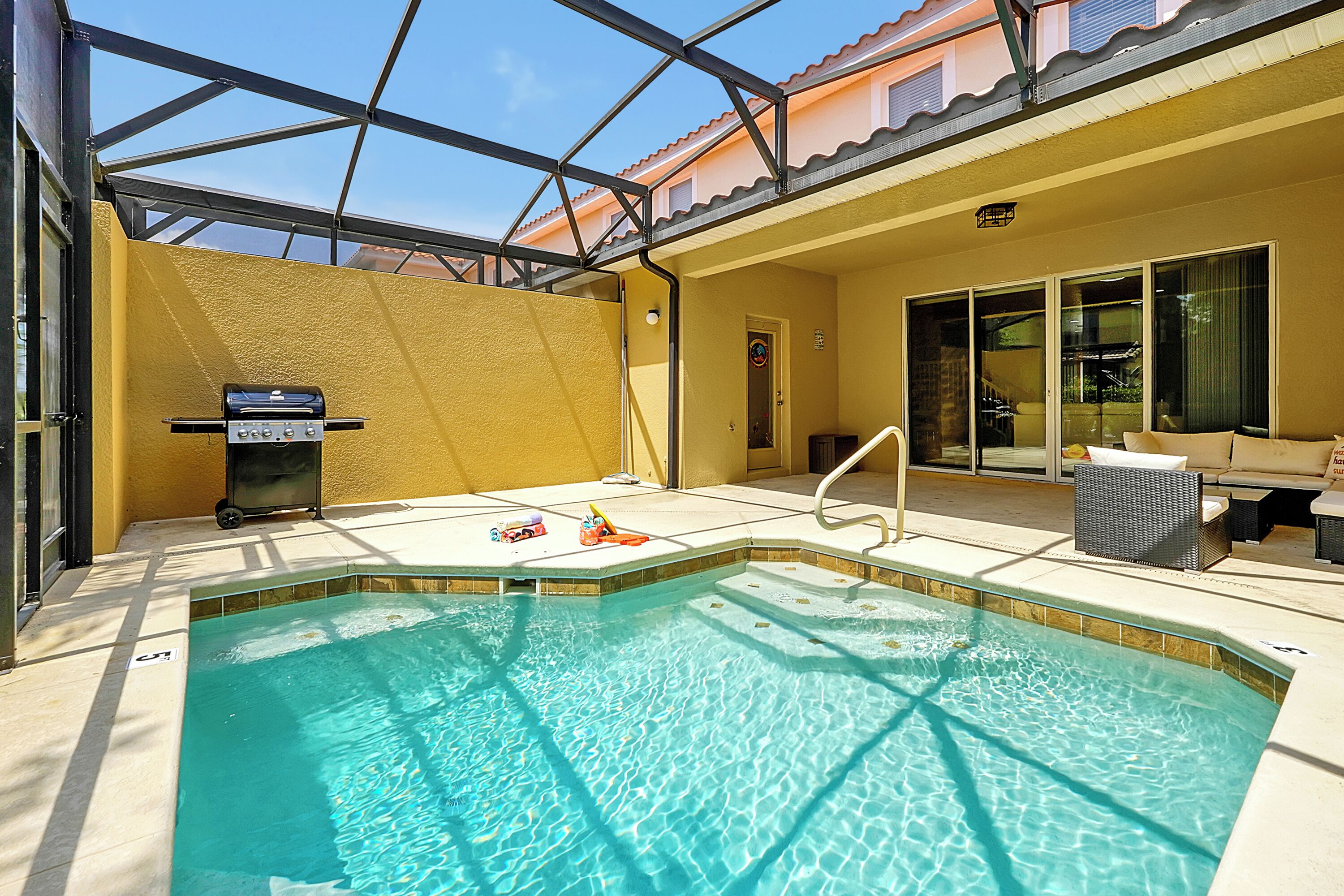 A swimming pool with a glass ceiling, a barbecue grill, and outdoor furniture.