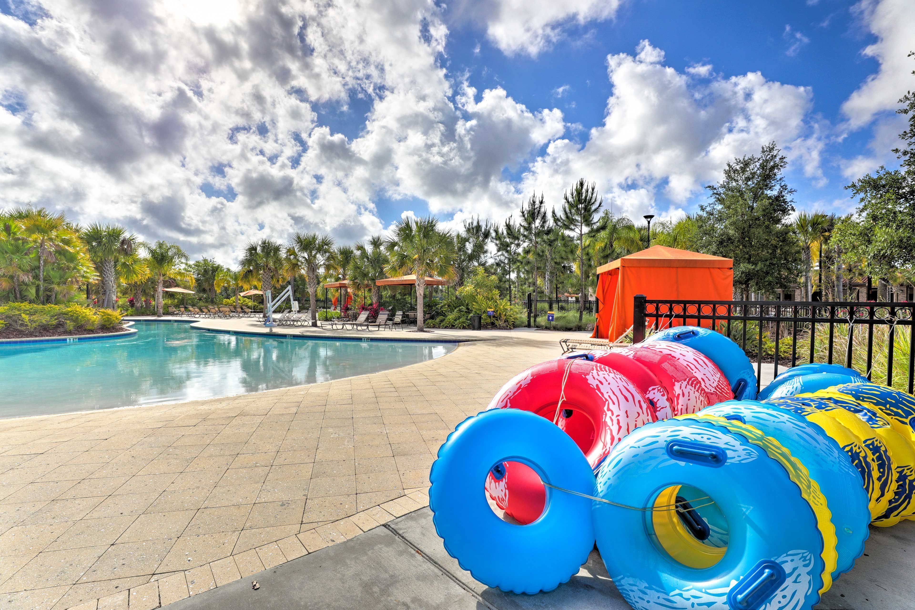 A swimming pool with inflatable rings, palm trees, and a fenced area with a red tent.