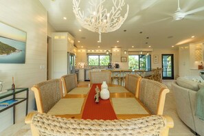 A spacious dining area with a long table, woven chairs, and a central chandelier.