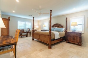 A four-poster bed with a wooden headboard, a dining table with chairs, and a cabinet with a lamp.