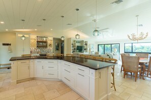 A spacious kitchen with a large island, white cabinetry, and a dining area with wicker chairs. - Camino Del Mar - Steps from the Beach! (Sanibel)