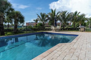 A rectangular swimming pool with clear blue water, surrounded by a brick deck and a metal fence. - Camino Del Mar - Steps from the Beach! (Sanibel)