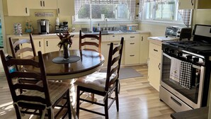 Une cuisine avec une table ronde, des chaises, un fourneau et une fenêtre avec des rideaux.