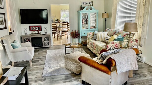 Un salon comprenant un canapé, un fauteuil et une table basse. Un téléviseur est fixé au mur, et il y a un meuble sur lequel est posée une pancarte indiquant « BIENVENUE ».