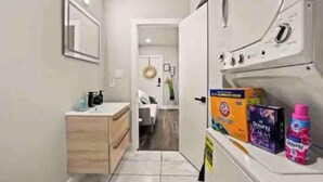 Un pasillo estrecho con una lavadora, un mueble pequeño y una puerta que da a un dormitorio.