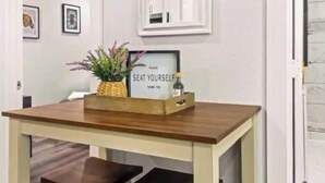 A dining table with a wooden top and a bench, a framed sign with the text "PLEASE SEAT YOURSELF," and a small plant in a wooden box.