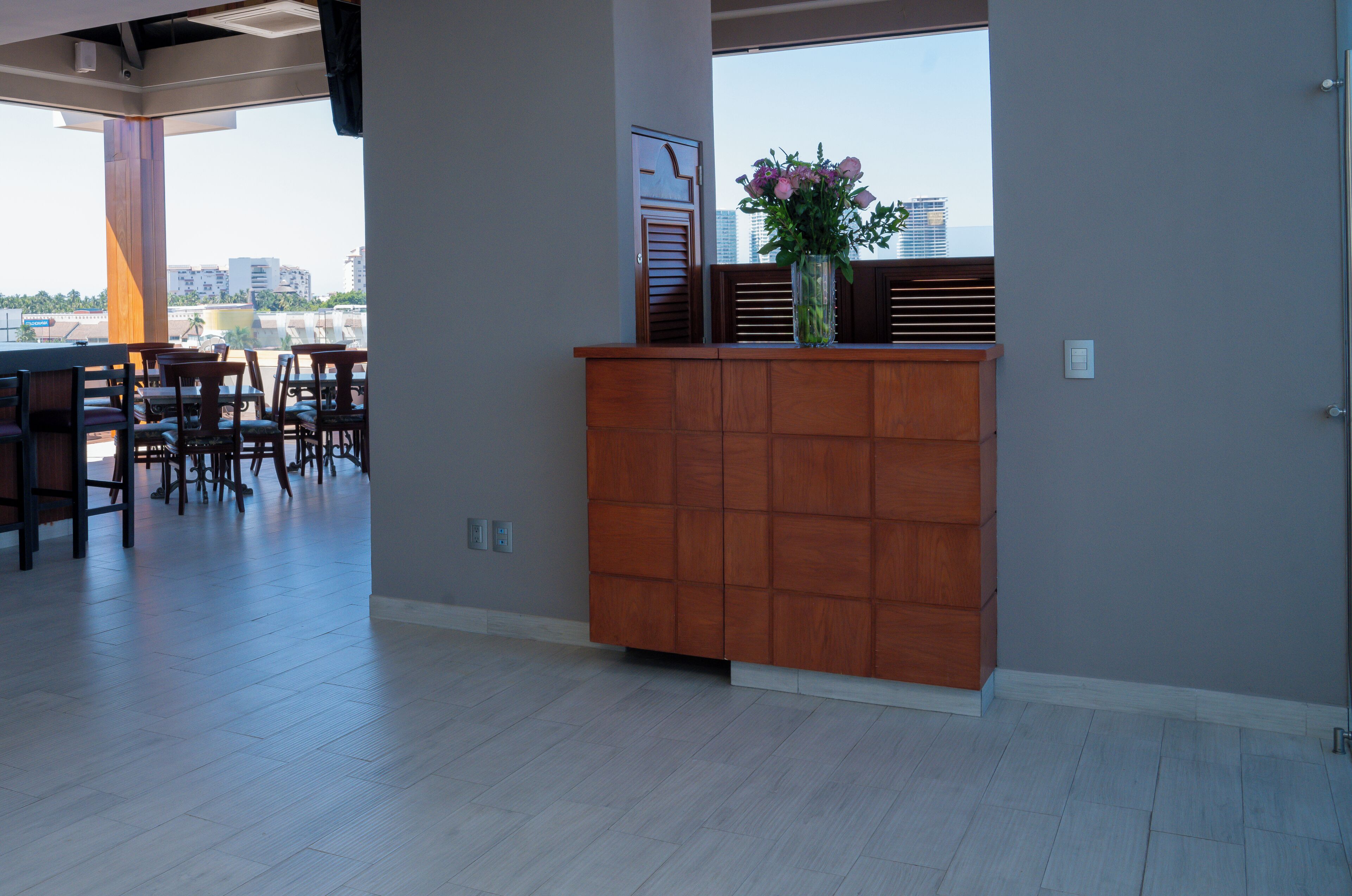 A spacious room with a wooden reception desk, a large window with a view of buildings, and a seating area with chairs.