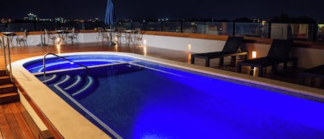 Zwembad op het dak met blauw verlichte rand, houten terras, lounge fauteuils en tafels.