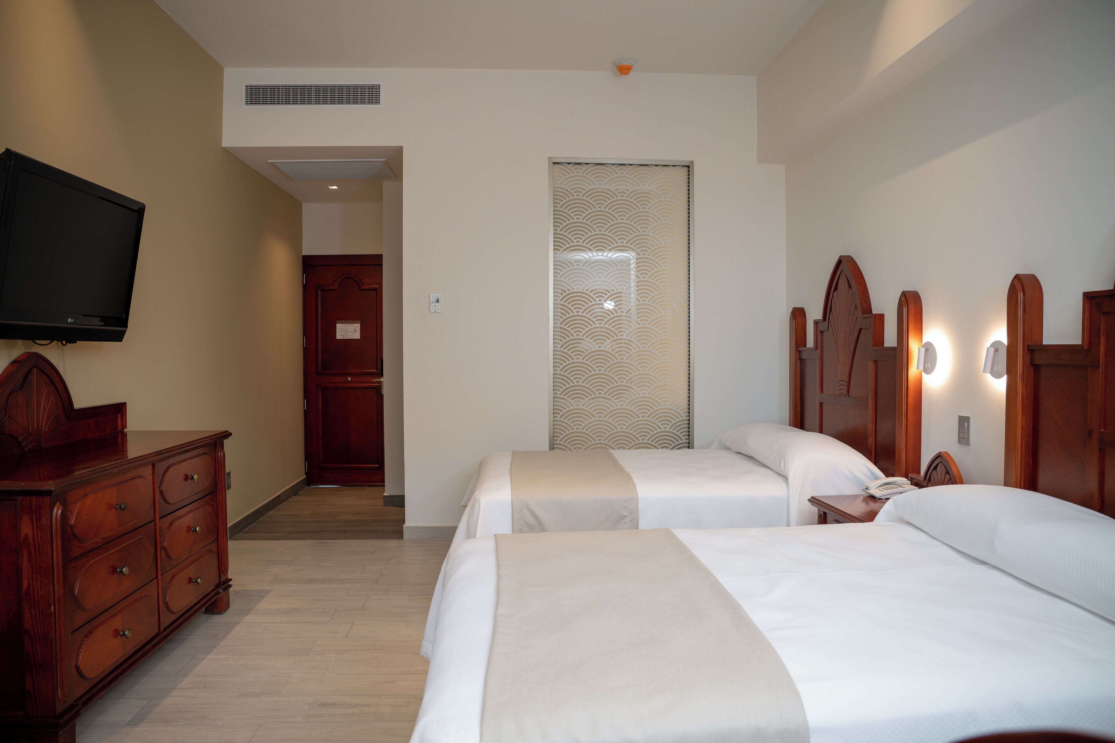 Habitació d'hotel amb dos llits, una televisió, un taulell de fusta i una porta que dóna a una altra habitació.