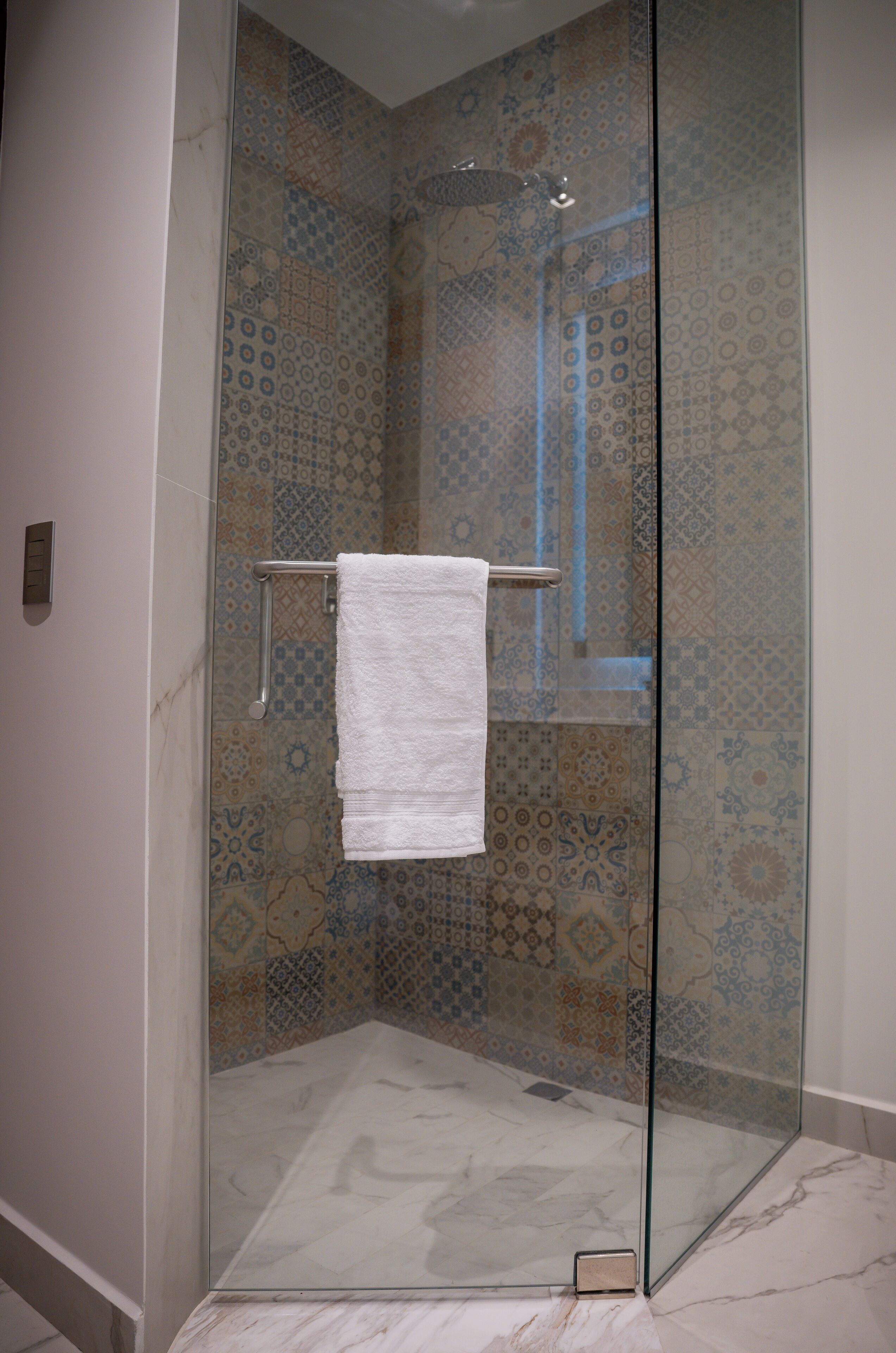Une douche fermée par des parois de verre, avec une serviette blanche suspendue à un porte-serviettes en métal.