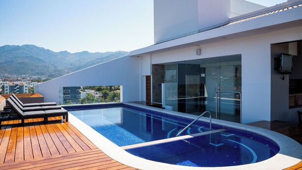 Una piscina moderna en la azotea con terraza de madera, paredes de vidrio y vistas a las montañas.