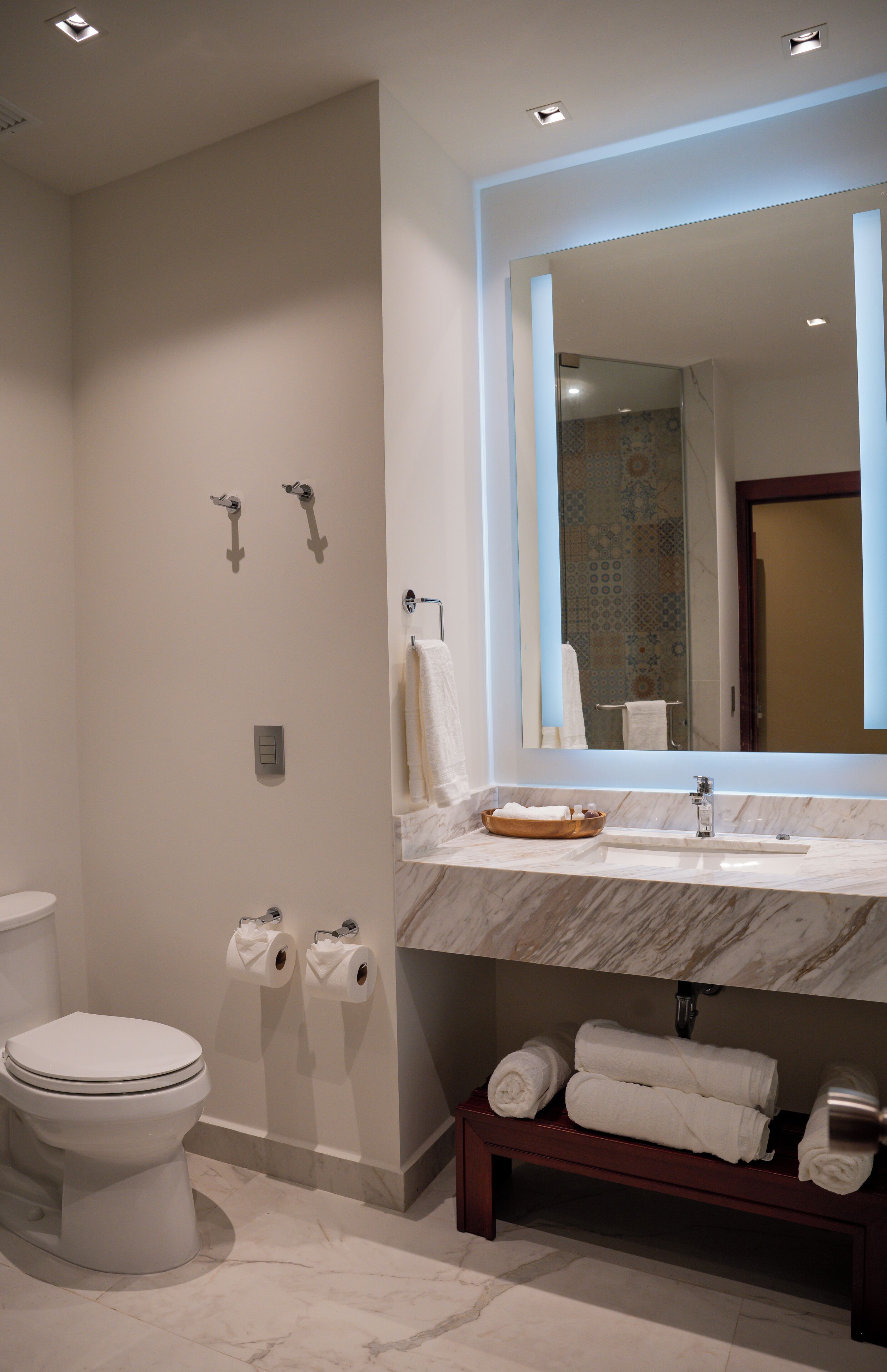Un baño moderno con inodoro, lavabo de encimera de mármol, espejo y toallero.