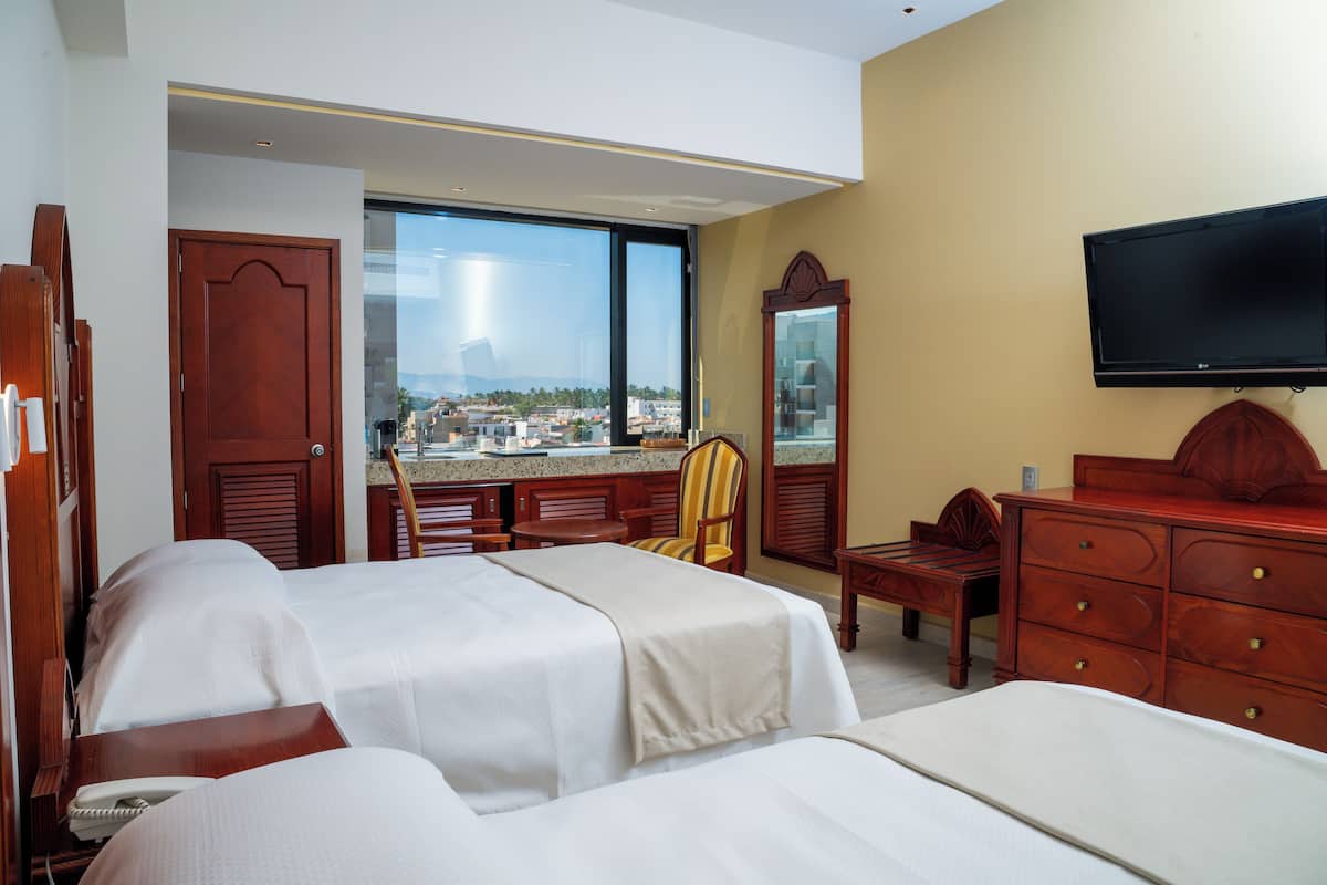 Quarto de hotel com duas camas, televisão, escrivaninha e uma cadeira.