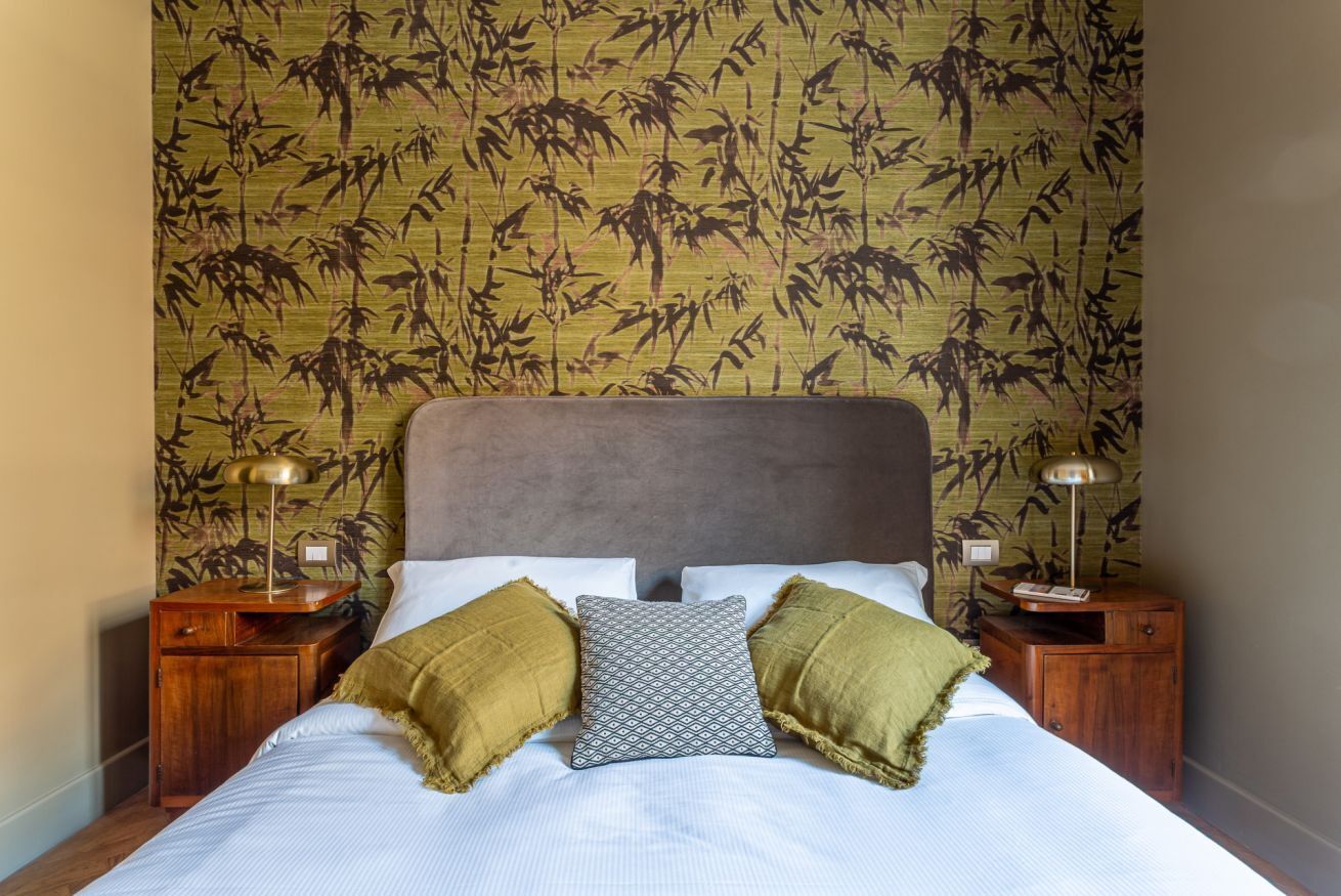 A bed with a headboard, two bedside tables, and a patterned wall.