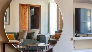 Een woonkamer met een bank, fauteuil, salontafel en een grote spiegel die de ruimte weerspiegelt.