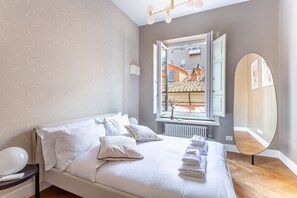 A bedroom with a bed, pillows, a bedside table, a window with a view, and a mirror.
