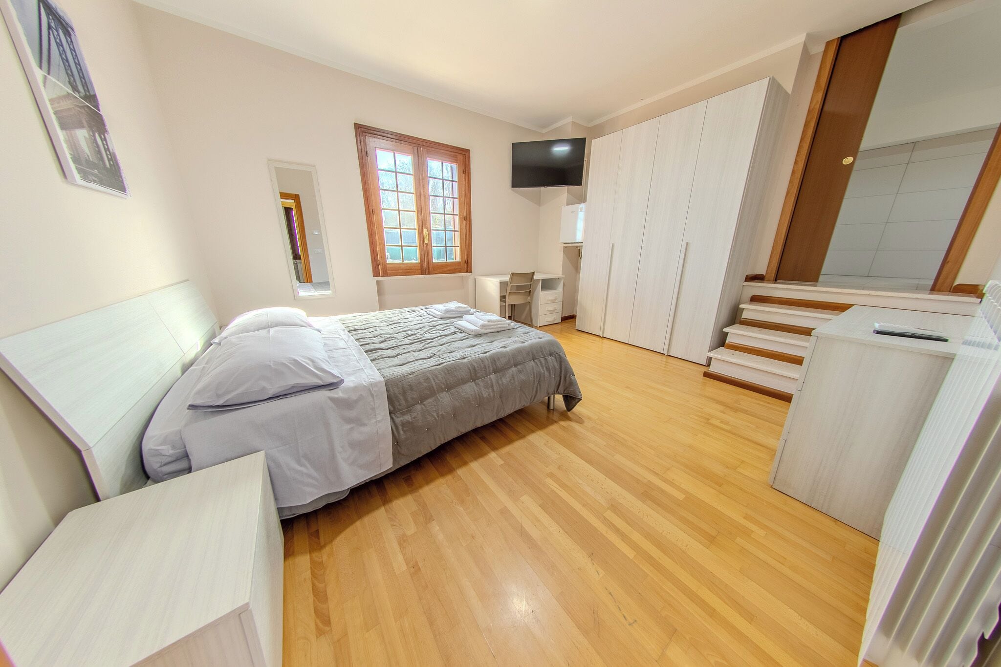 A bedroom with a bed, a desk, a TV, and a wardrobe.