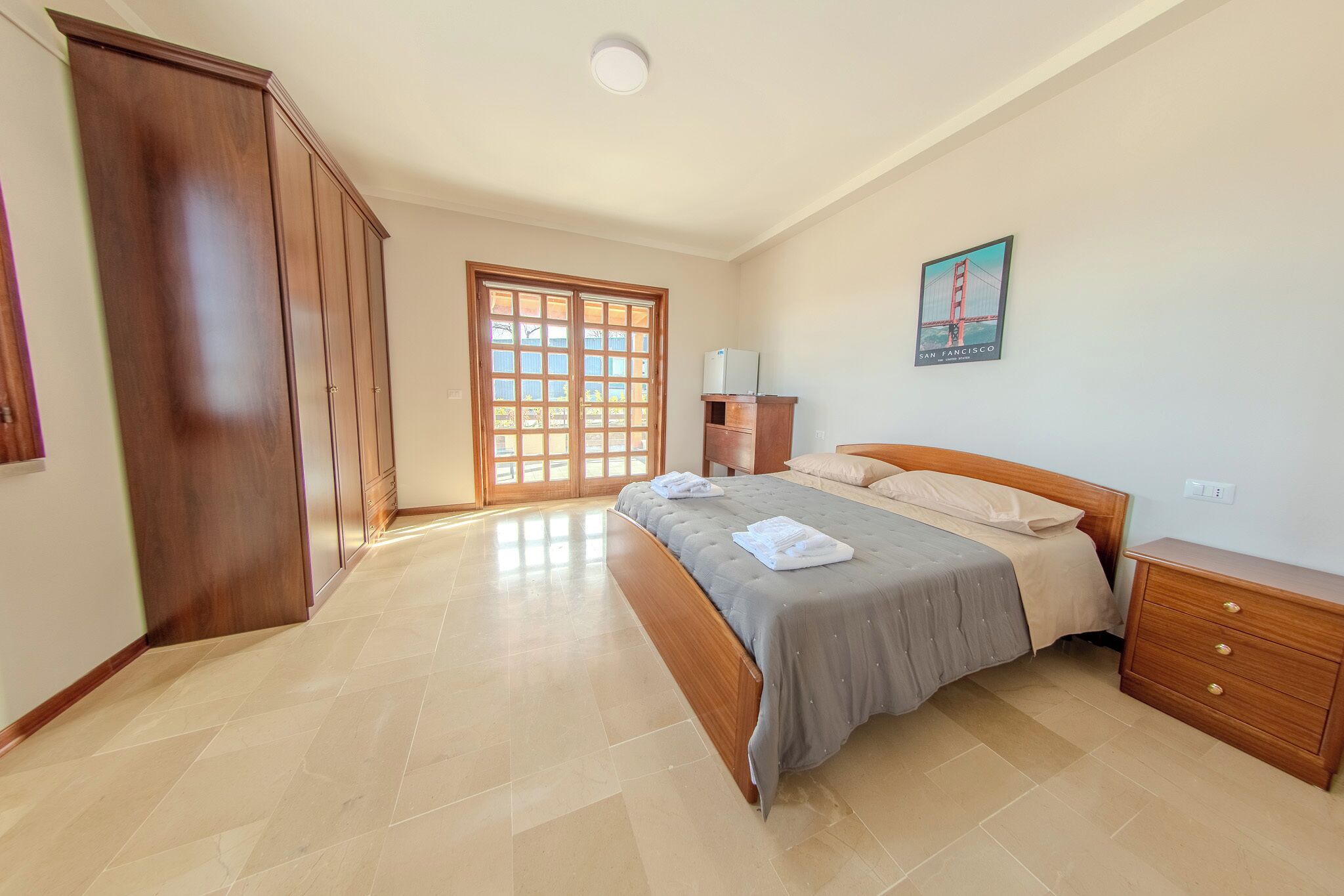 A bedroom with a bed, wooden wardrobe, a nightstand, and a door with a view.
