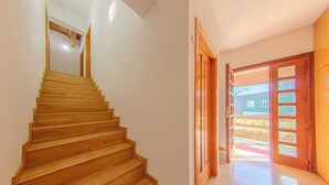 A wooden staircase leading to a landing with a view of a green building outside.