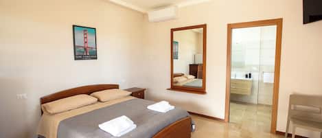 A hotel room with a bed, a mirror, a wooden chair, and a bathroom visible through an open door.