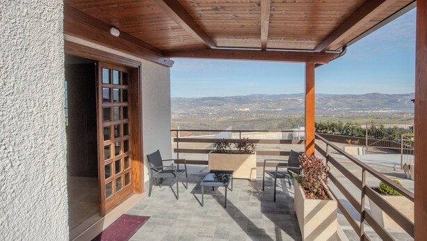 A covered outdoor seating area with a wooden ceiling, a view of distant mountains, and a door leading to the interior.