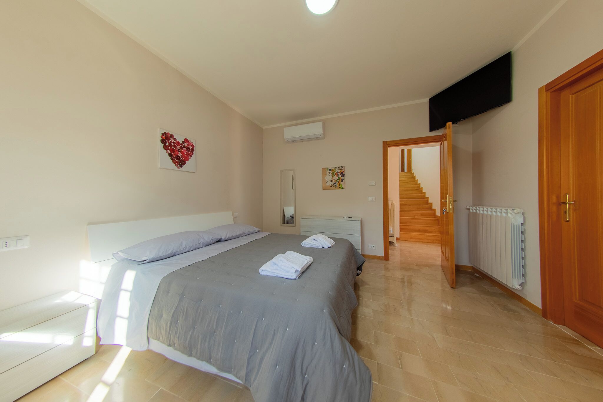 A bedroom with a bed, bedside tables, a mirror, a staircase, and a door.