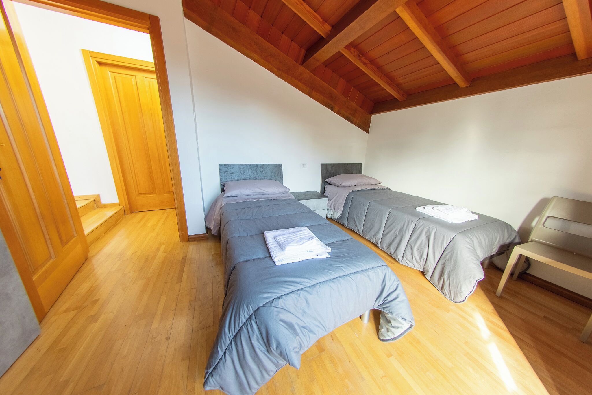 Habitación con dos camas, suelo de madera y techo alto.