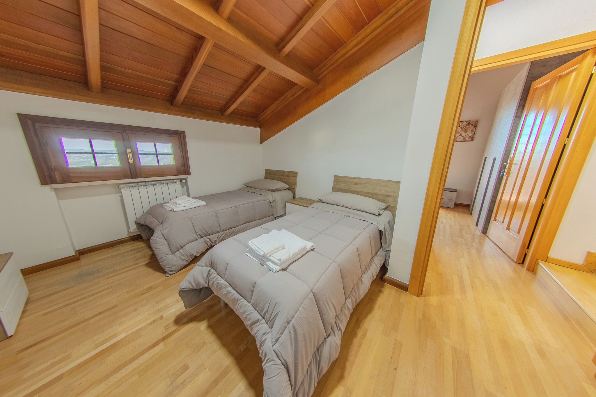 Une chambre avec deux lits, un plancher en bois, un plafond en pente et une fenêtre laissant filtrer une lumière violette.