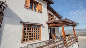 A two-story house with a balcony, wooden shutters, and a view of the landscape.