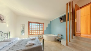 A bedroom with a bed, a window, a bathtub, and a wooden staircase.