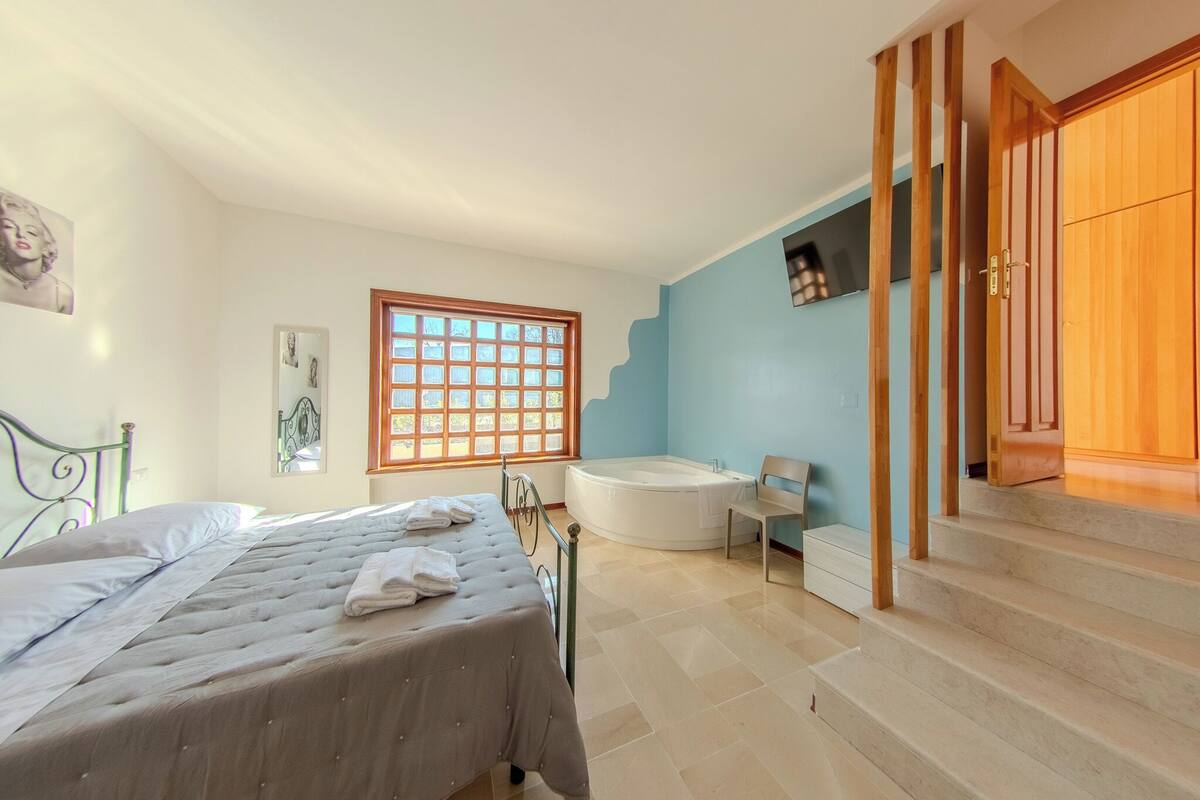 Ein Schlafzimmer mit Bett, Fenster, Badewanne und einer Holztreppe.