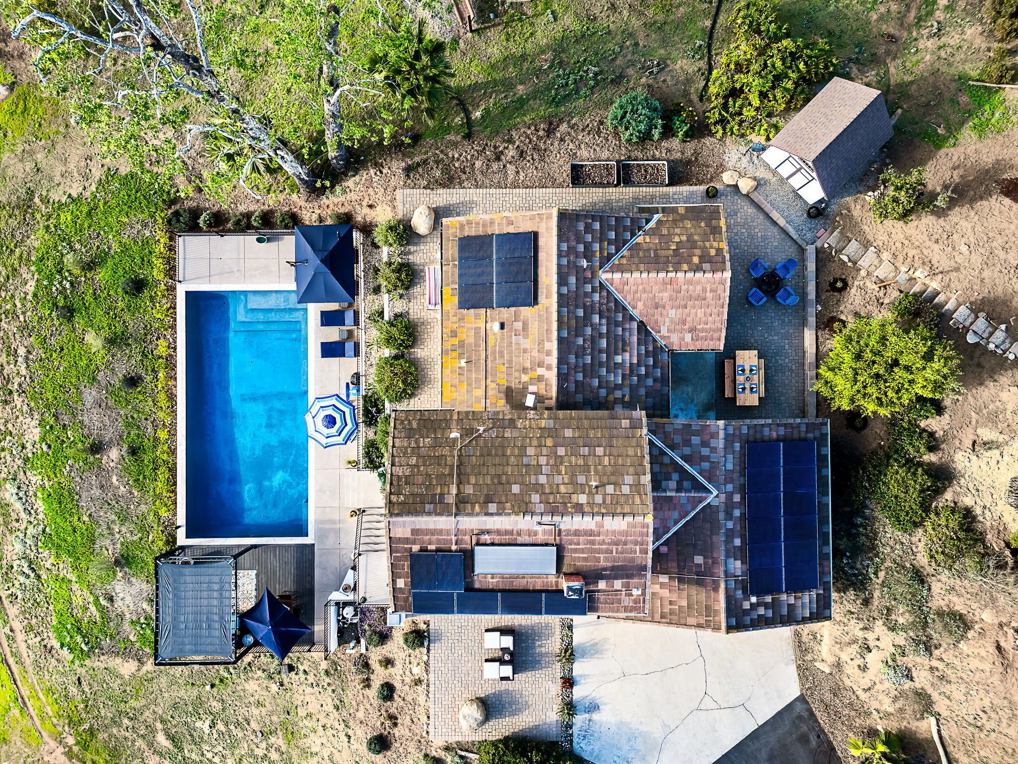 An aerial view of a property with a swimming pool, outdoor seating area, and solar panels.