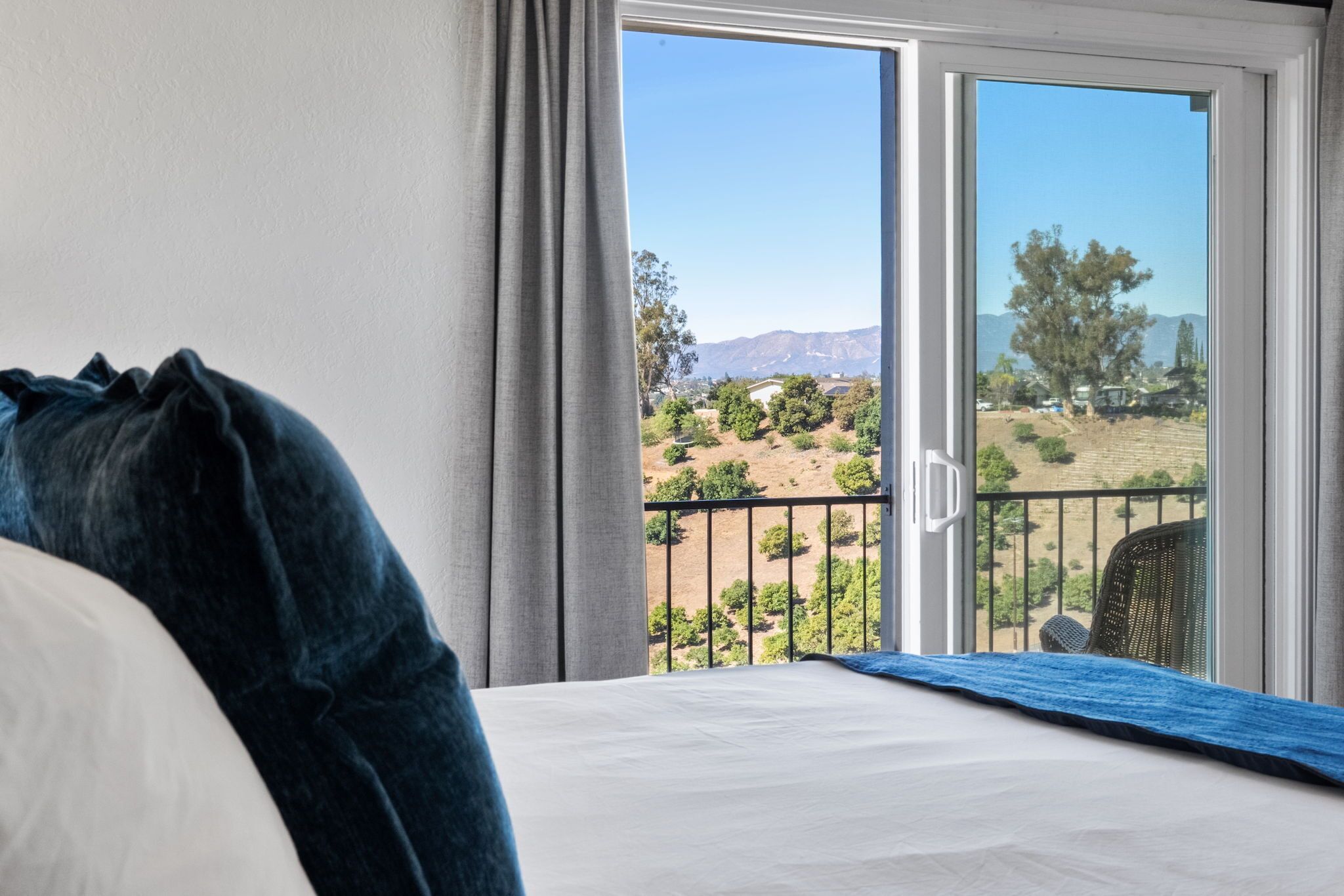 A hotel room with a bed, a view of a balcony, and a landscape with trees and mountains.